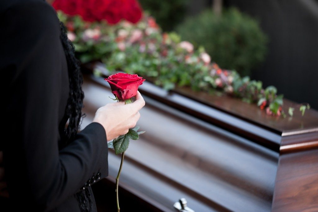 woman holding a rose near a coffin