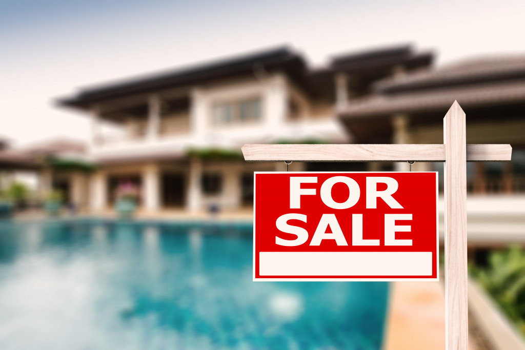 big modern house with pool in the yard with for sale signage in front of it