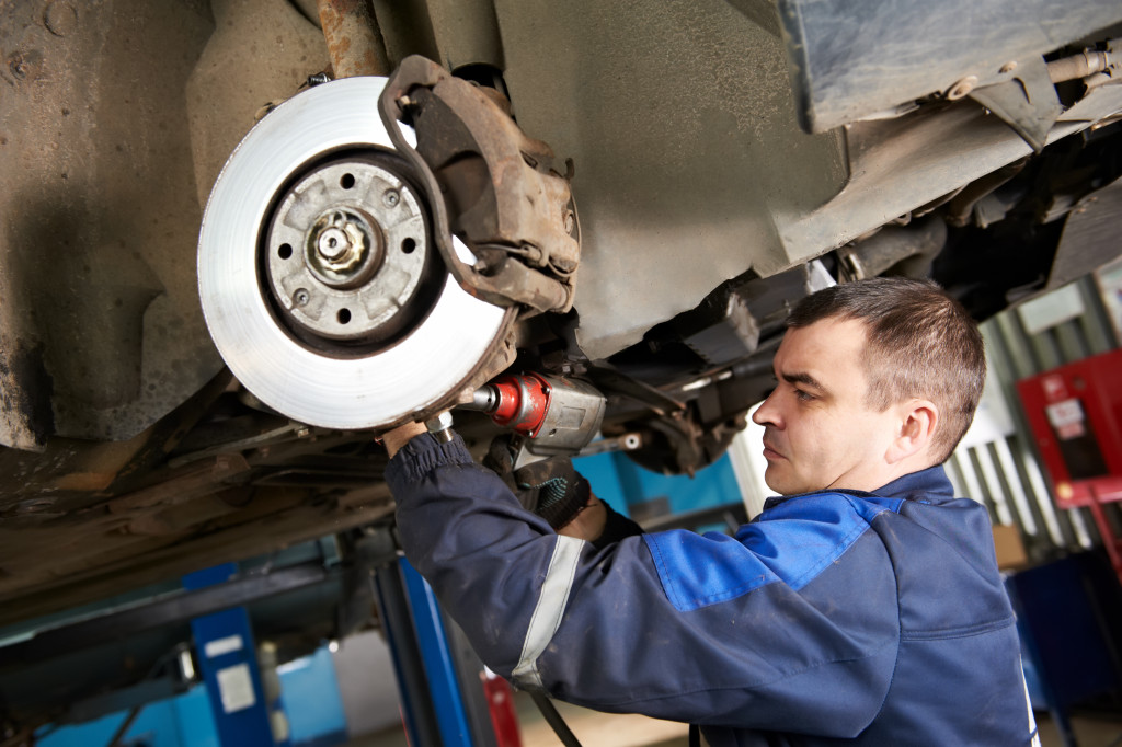 car mechanic examining car suspension of lifted automobile at repair service station