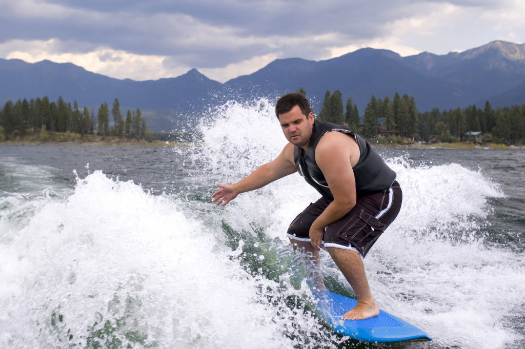 Man surfing with a blue surf board on the wake of a boat.