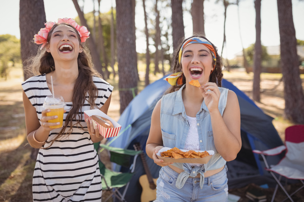 Portrait of two friends eating snack and drinking soft drinks on a camping trip 