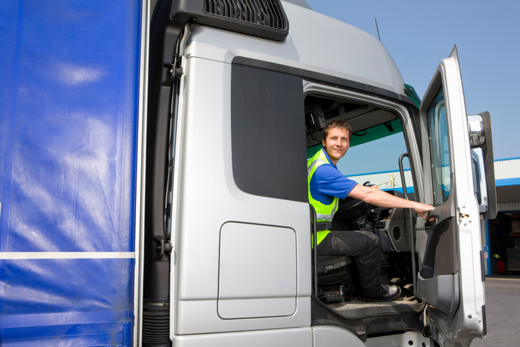 A wide shot of Truck driver sitting behind the wheel in a cab of semi-truck looking straight at the camera while closing the door