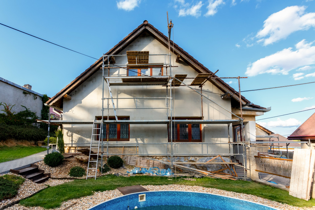 The exterior of a house being renovated. Scaffolding and construction materials are seen surrounding the facade of the building.