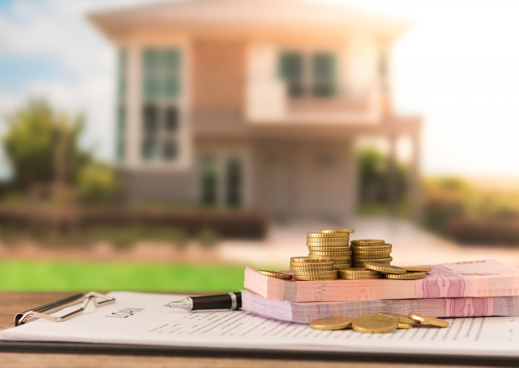 Stacks of money, a loan document, and a pen in front of a house