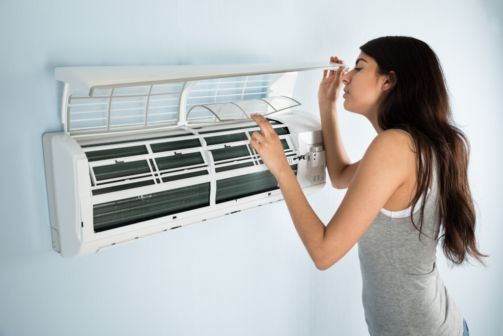 Young woman checking and cleaning the filters of an air conditioner at home.