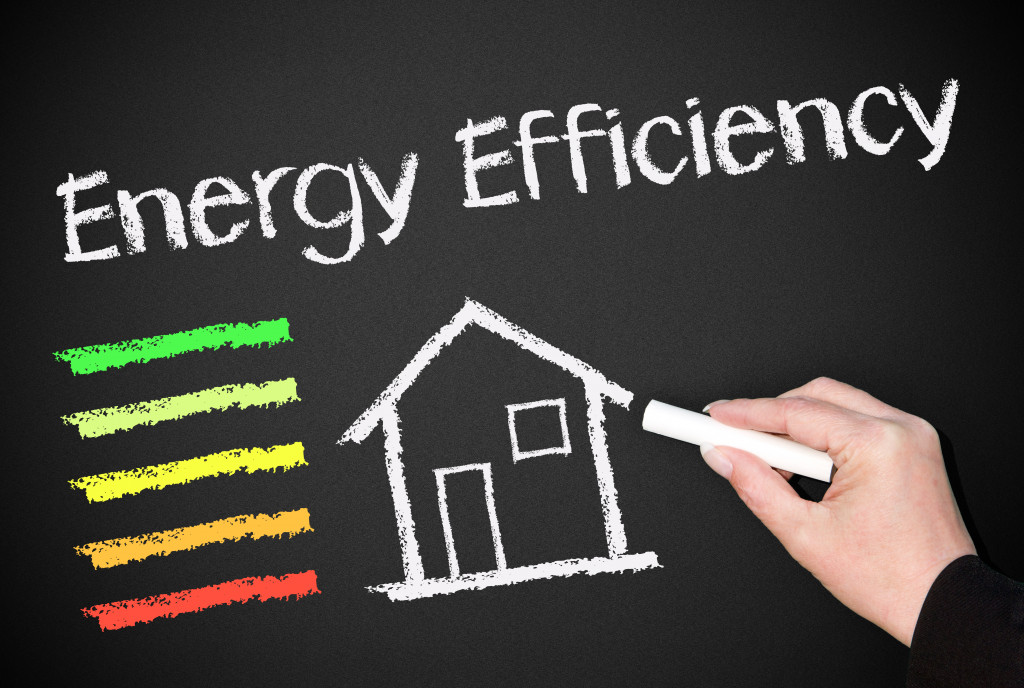 A person writing the words energy efficiency and drawing a house on a blackboard.