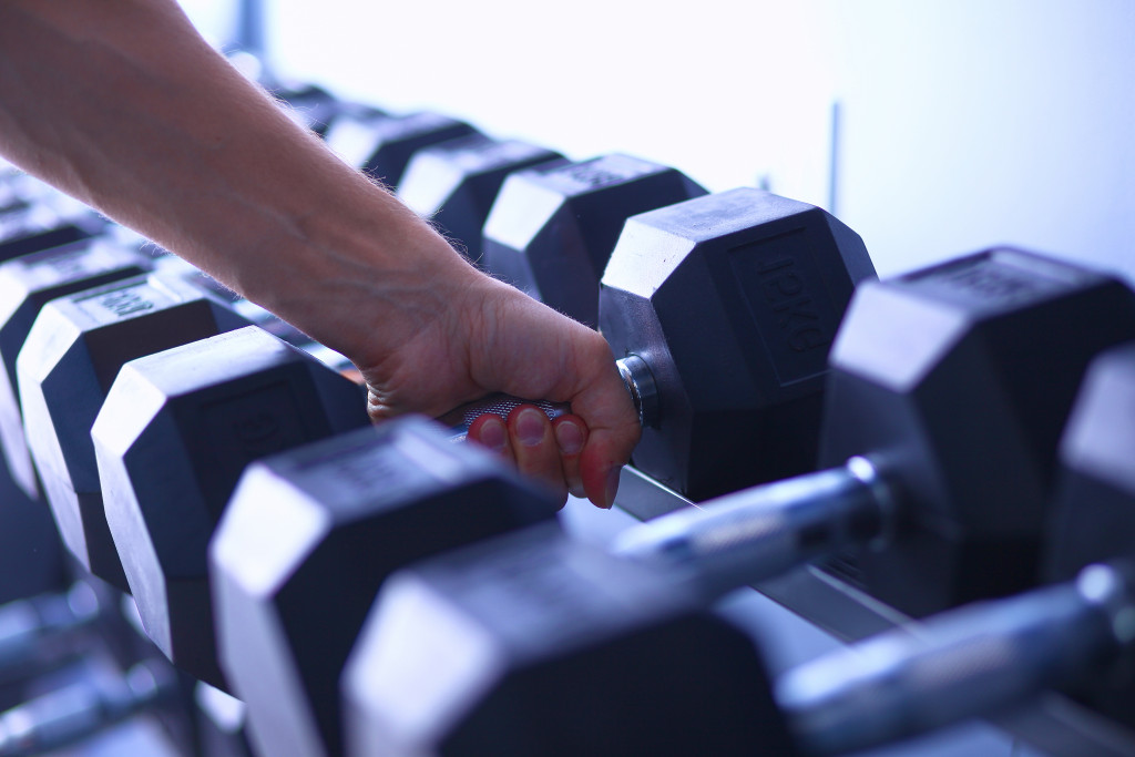 A hand taking up a dumbbell from the rack in a gym