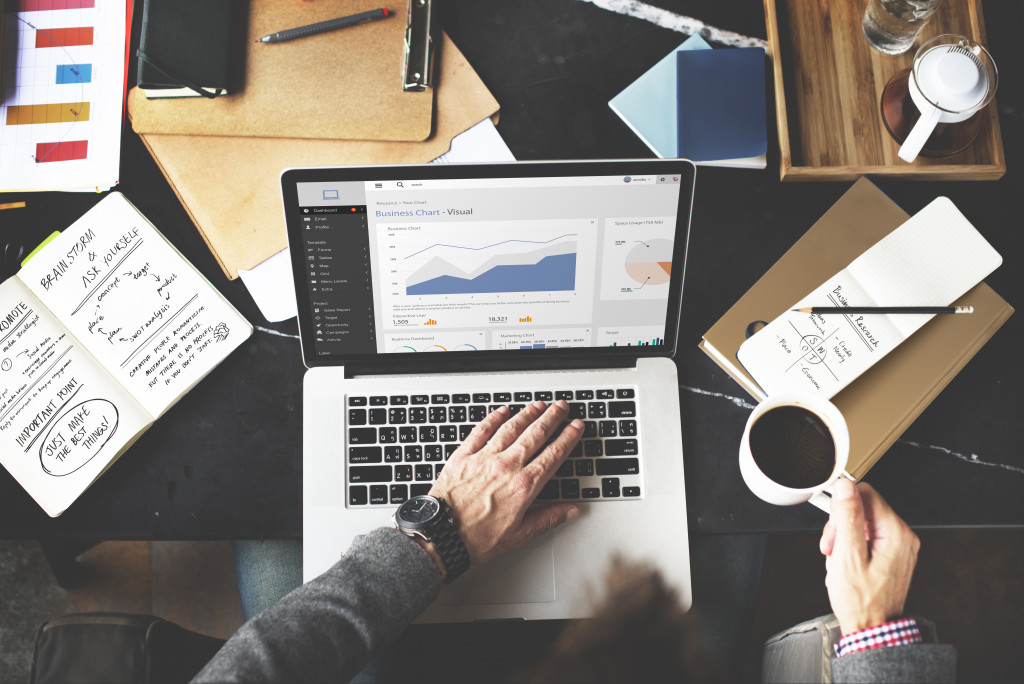 businessman using laptop to track profits with mug on one hand