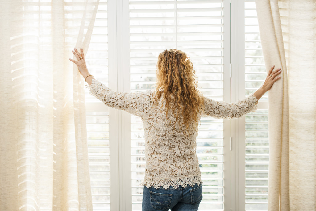 A woman parting the curtains to let in natural light