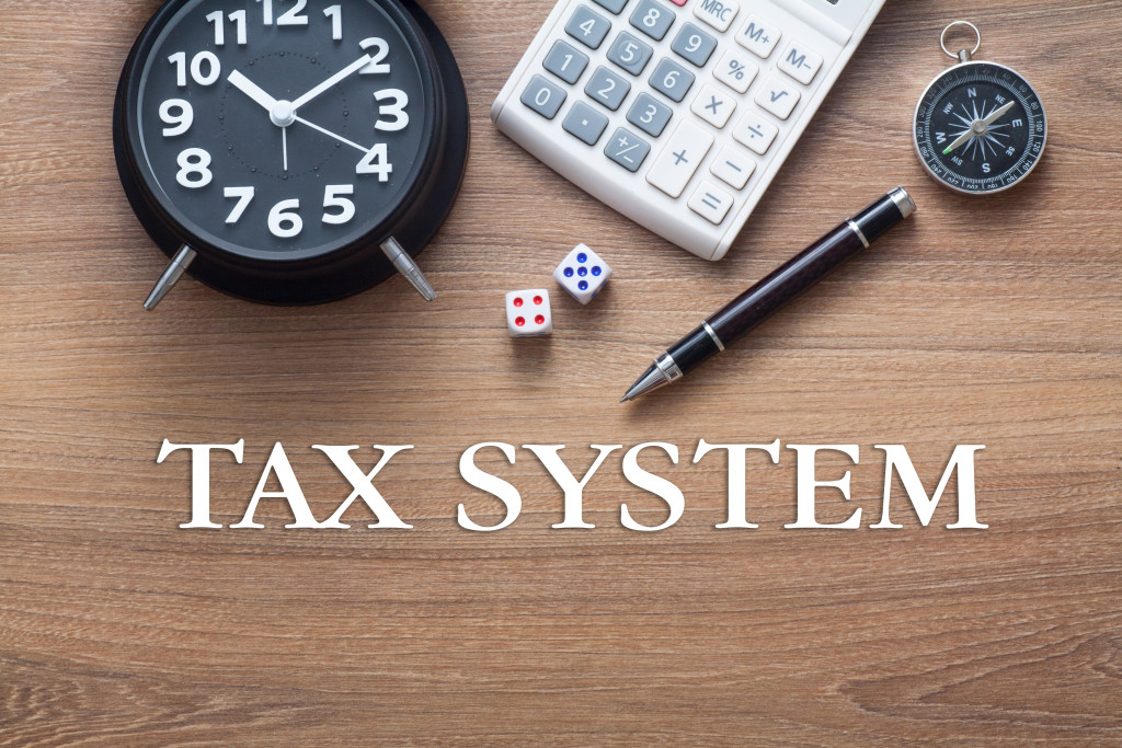 Term tax system above a table with a clock, calculator, dice, pen, and compass.