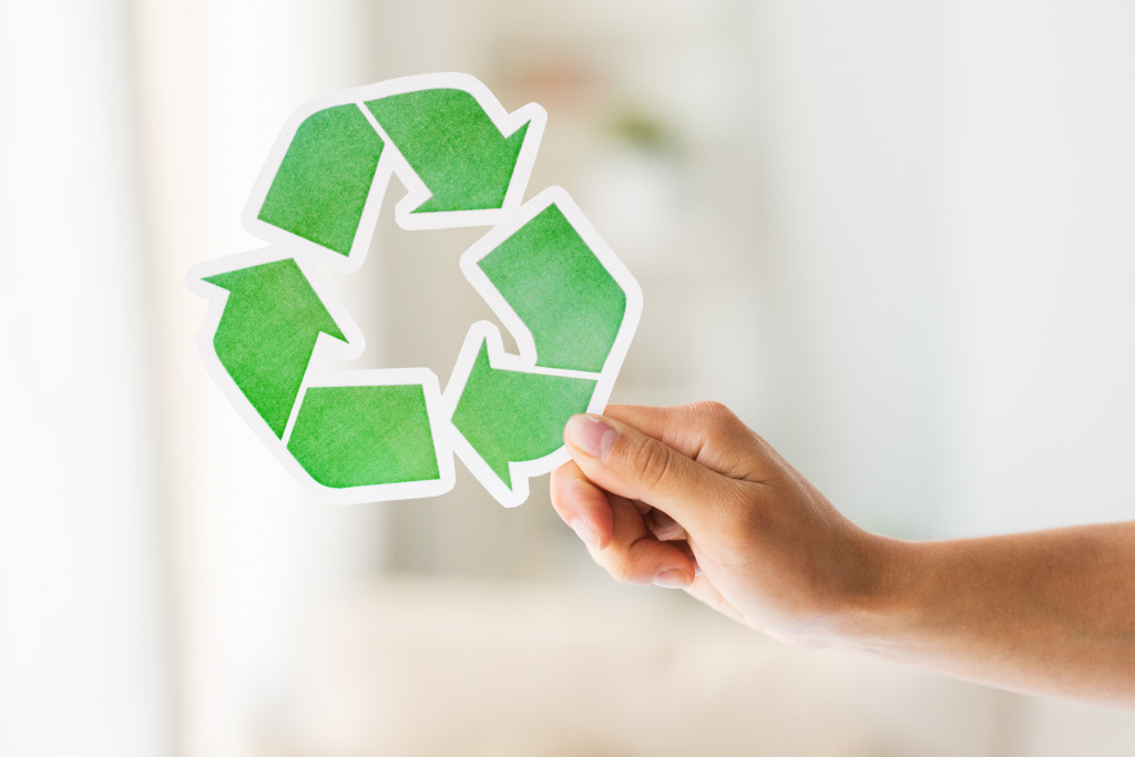 A hand holding a cutout of the recycling sign