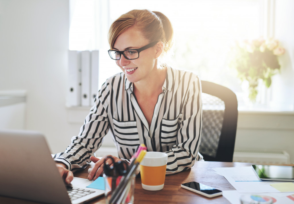 smiling woman with glasses working in her office on her desk and laptop